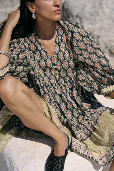 Close-up of woman seated outdoors wearing the Daughters of India Bhoomi Mini Dress in Onyx, showing the detailed paisley block print fabric and tiered skirt with border hem