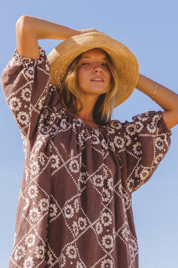 Dahlia Mini Dress Maple — model with straw hat looking up, arm raised, showing hand block print linen mini with diamond daisy motif, maple brown artisan print | Daughters of India