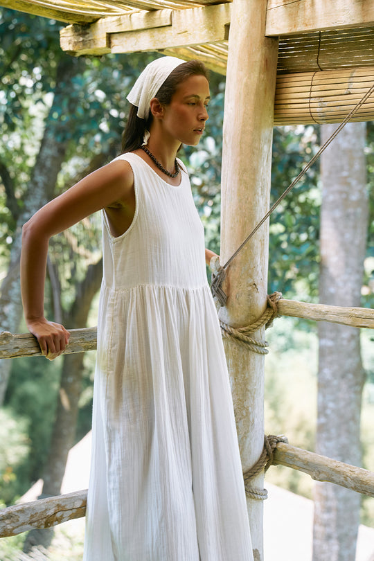 Nadi Dress White — side profile on tropical balcony, white double gauze cotton midi dress showing flowing silhouette, bamboo railing and greenery | Daughters of India