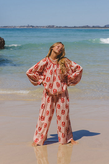 Ria Pants Cherry Blossom — beach full length front view, model wearing cherry blossom hand block print cotton wide-leg pants on sandy shore, pink floral motif on cream, artisan Jaipur India | Daughters of India