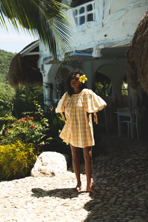 Freya Dress Honeycomb Plaid — full length outdoor shot by whitewashed villa, cobblestone path, flower in hair, handloom woven honeycomb yellow plaid mini dress, ethical artisan fashion | Daughters of India